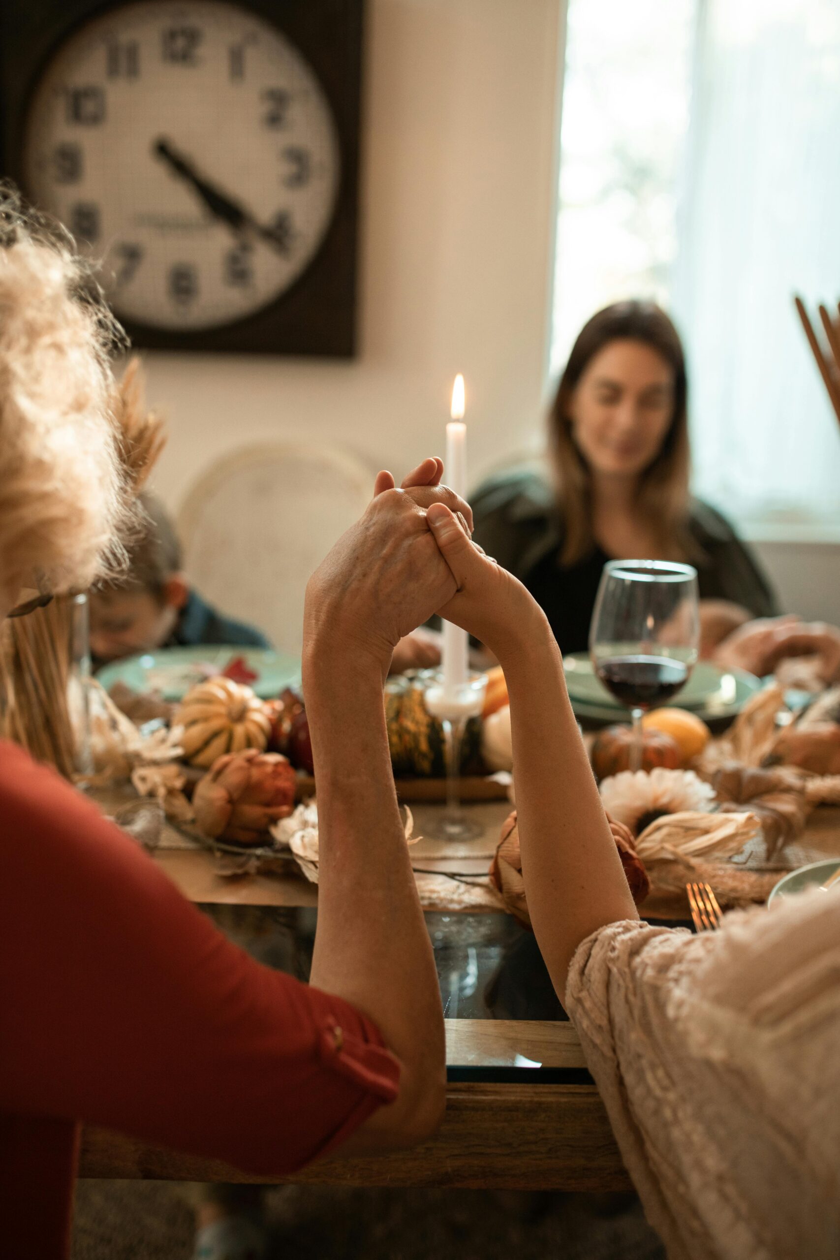 A family holding hands in prayer before a Thanksgiving dinner indoors with warm fall decor.
